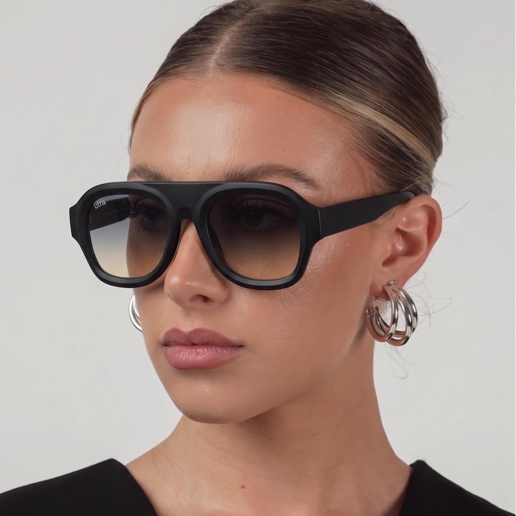 Femme portant les lunettes de soleil Montevia Osour Eyewear avec monture noire oversize et verres gris fumés dégradés.