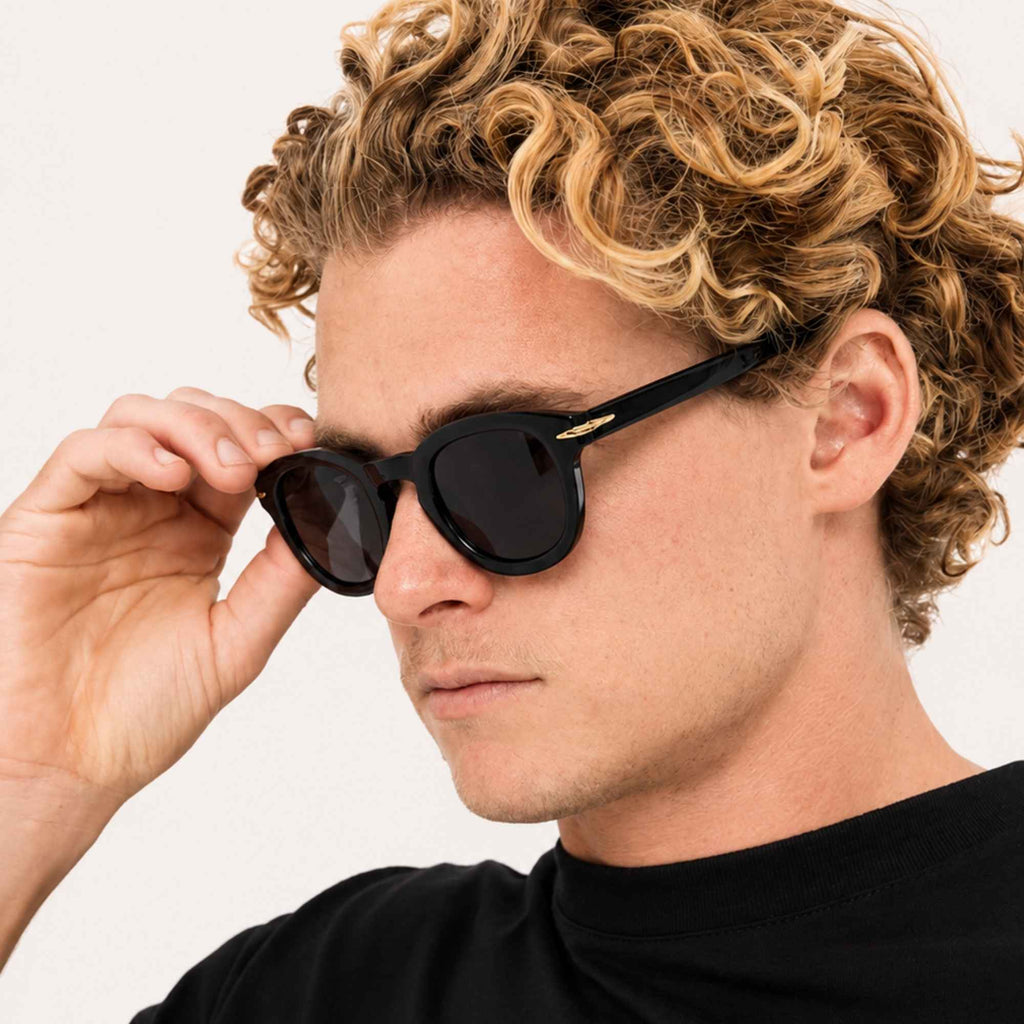 Homme portant les lunettes de soleil Niko Midnight noires Osour Eyewear avec monture ronde noire, détails dorés et verres noirs